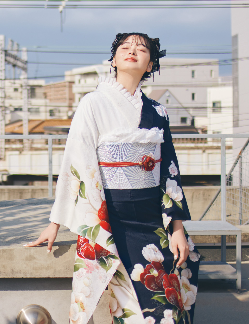 白×紺の切り替え振袖に赤・白・桃の花柄をあしらい、淡色の帯と赤の帯締を合わせた女性が、華やかな振袖姿を見せている様子。