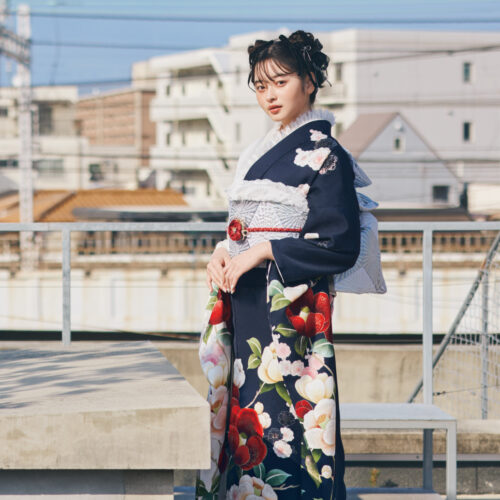 白×紺の切り替え振袖に赤・白・桃の花柄をあしらい、淡色の帯と赤の帯締を合わせた女性が、華やかな振袖姿を見せている様子。