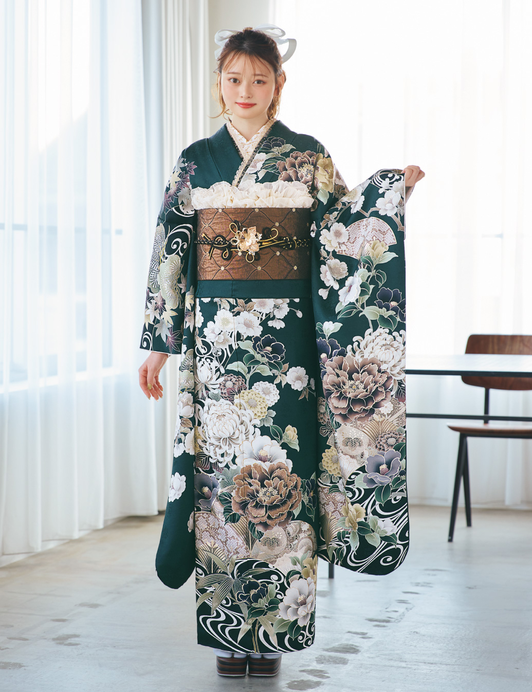 深緑の振袖に白・ベージュ・淡紫の花柄をあしらい、茶系の帯と金黒の帯締を合わせた女性が、上品で華やかな振袖姿を見せている様子。