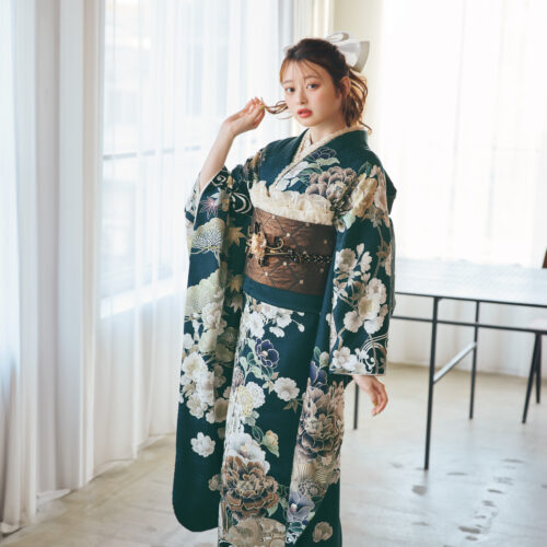 深緑の振袖に白・ベージュ・淡紫の花柄をあしらい、茶系の帯と金黒の帯締を合わせた女性が、上品で華やかな振袖姿を見せている様子。