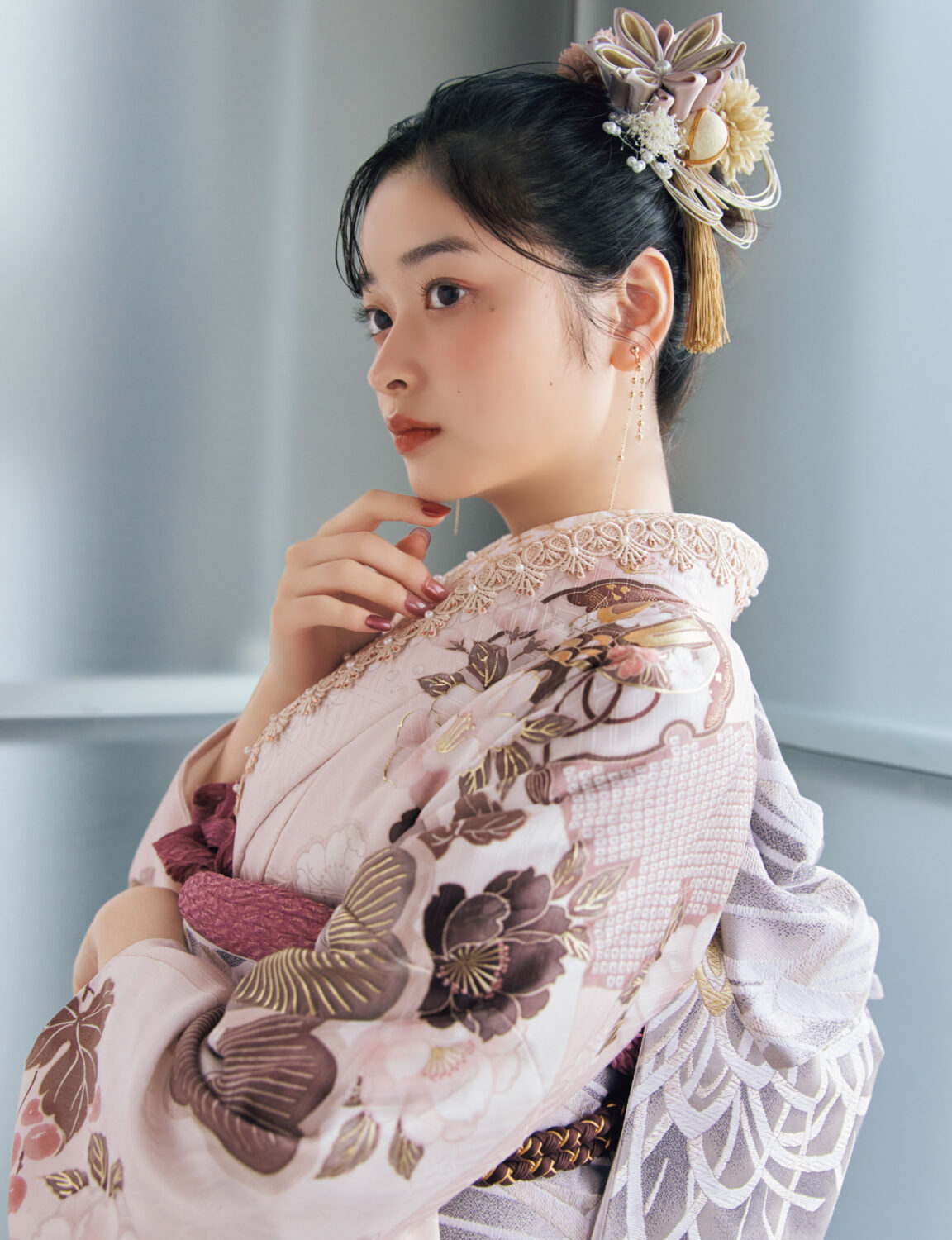 淡桃色の振袖に白・金・茶・モーブの花柄をあしらい、淡灰の帯と紫の帯締を合わせた女性が、優美で上品な振袖姿を見せている様子。