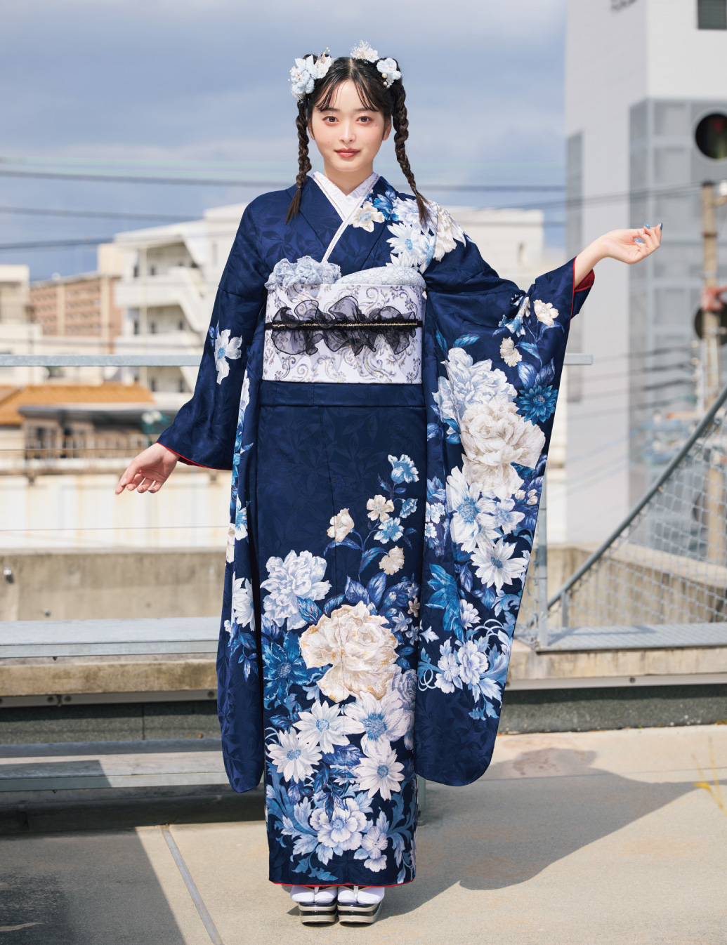 深紺の振袖に白・水色・ベージュの花柄をあしらい、白帯と黒リボンの帯締を合わせた女性が、上品で都会的な振袖姿を見せている様子。