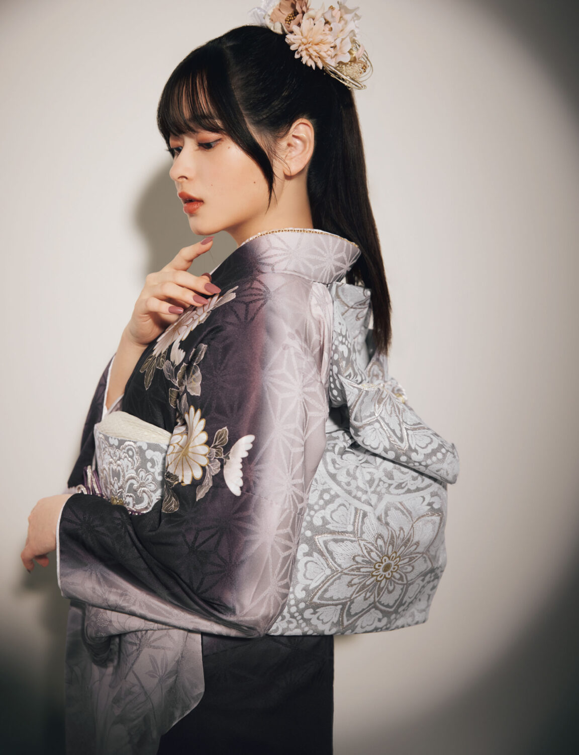 灰紫のグラデーション振袖に白・金・桃・紫の花柄をあしらい、淡灰の帯と紫の帯締を合わせた女性が、上品で華やかな振袖姿を見せている様子。