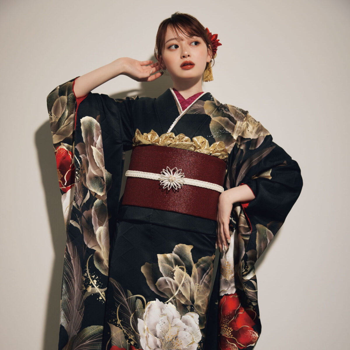 黒地に金・白・赤の花柄をあしらい、深紅の帯と白の帯締を合わせた女性が、重厚で華やかな振袖姿を見せている様子。