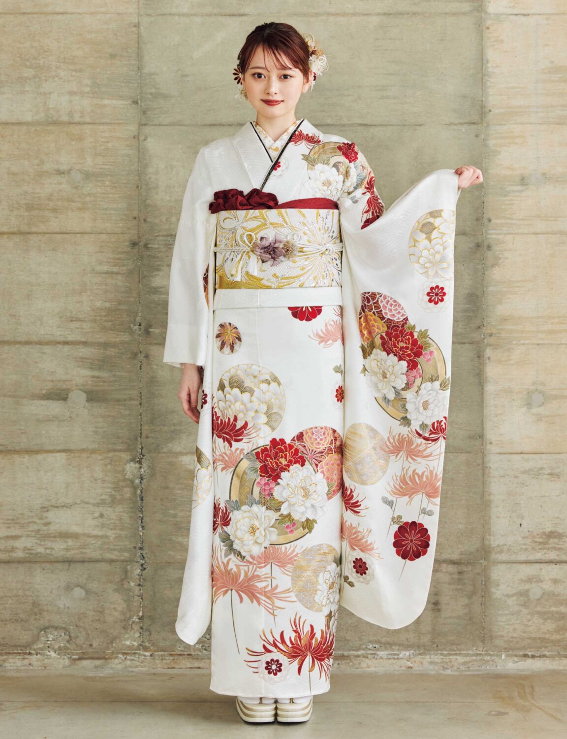 白地に赤・金・ベージュの花柄をあしらい、金白の帯を合わせた女性が、上品で華やかな古典振袖姿を見せている様子。
