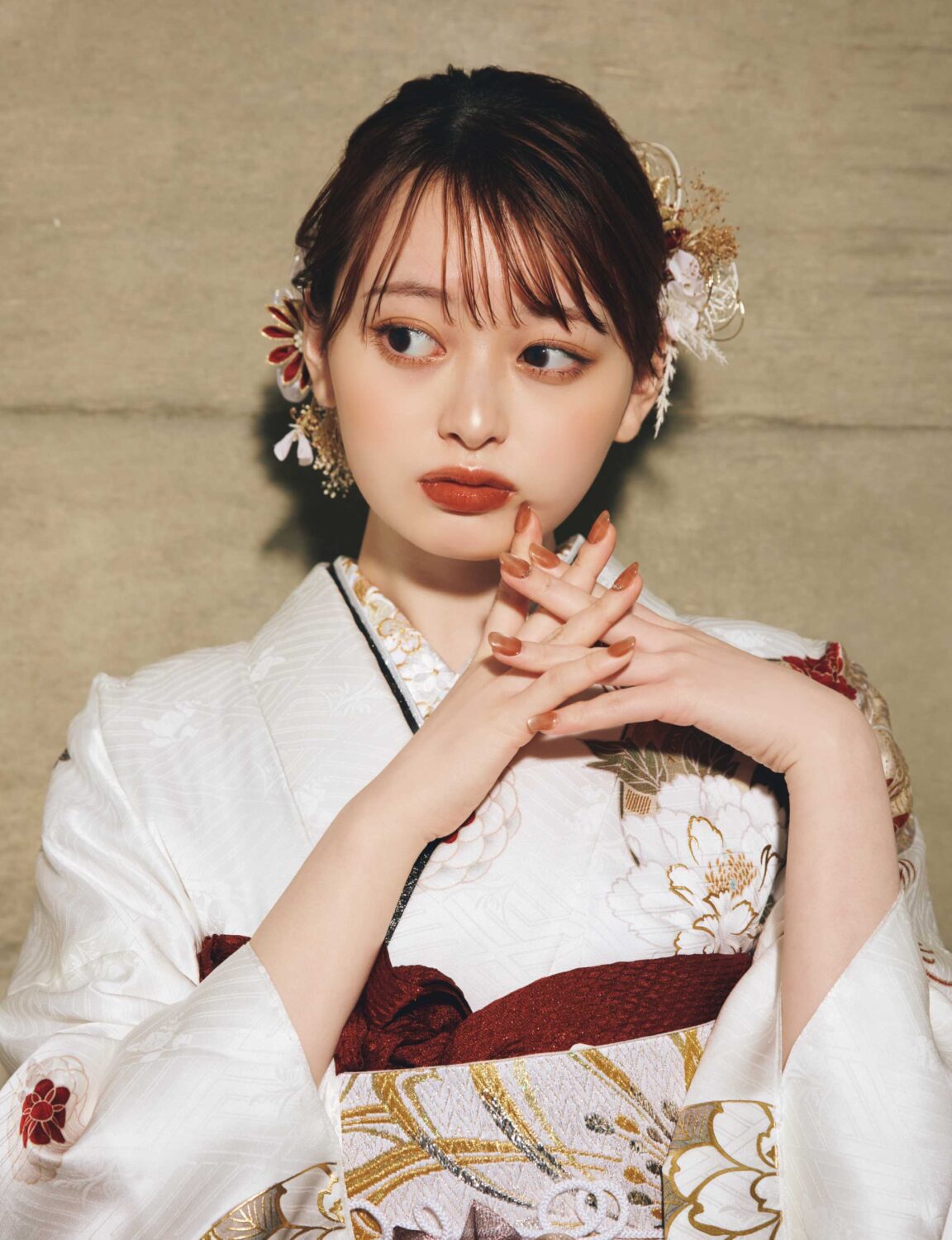 白地に赤・金・ベージュの花柄をあしらい、金白の帯を合わせた女性が、上品で華やかな古典振袖姿を見せている様子。