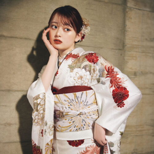 白地に赤・金・ベージュの花柄をあしらい、金白の帯を合わせた女性が、上品で華やかな古典振袖姿を見せている様子。