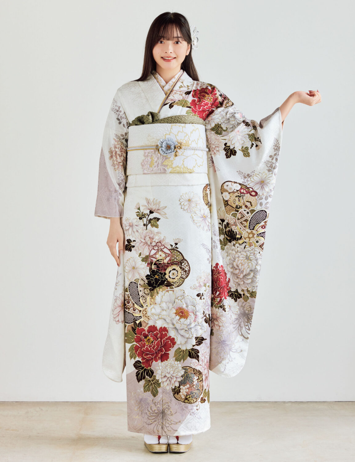 白地の振袖に赤・金・緑・ベージュの花柄をあしらい、淡色の帯と花の帯飾りを合わせた女性が、上品で華やかな振袖姿を見せている様子。