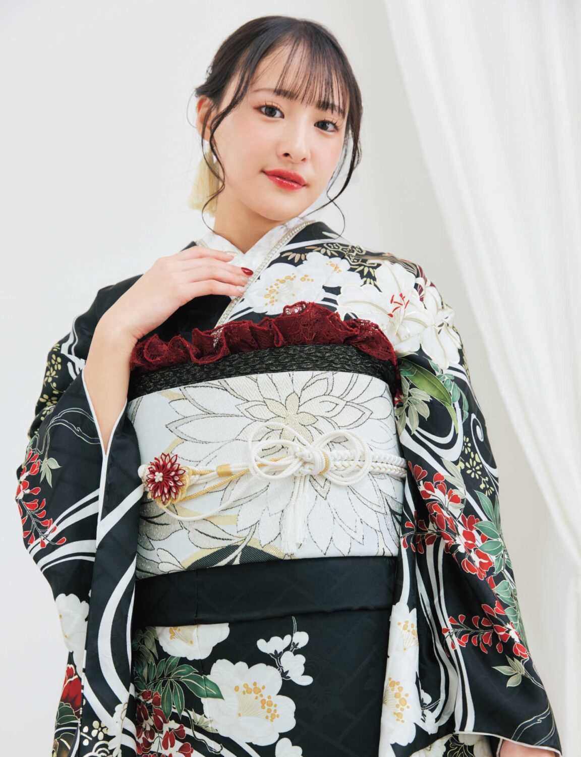 黒地の振袖に白・赤・緑・金の花柄をあしらい、淡色の帯を合わせた女性が、重厚で華やかな振袖姿を見せている様子。