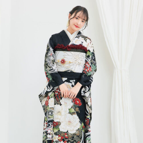 黒地の振袖に白・赤・緑・金の花柄をあしらい、淡色の帯を合わせた女性が、重厚で華やかな振袖姿を見せている様子。