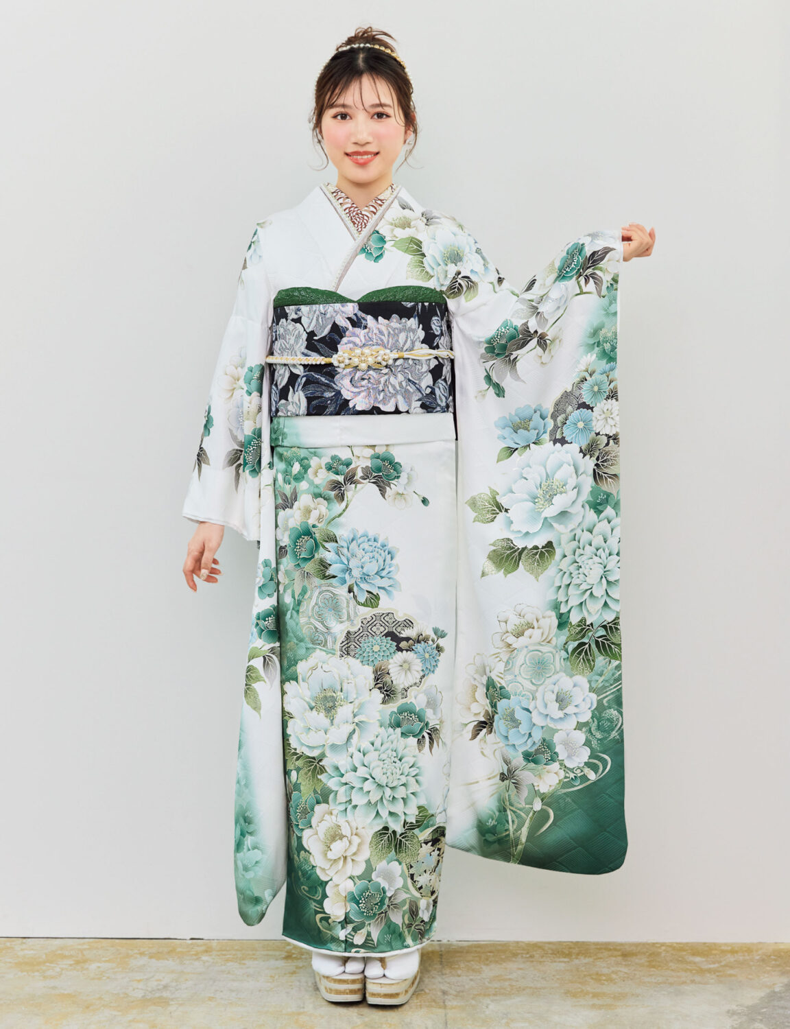 白地の振袖に緑・青・水色の花柄をあしらい、黒地の帯を合わせた女性が、爽やかで上品な振袖姿を見せている様子。