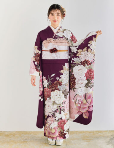 深紫の振袖に白・桃・金の花柄をあしらい、淡色の帯とレース装飾を合わせた女性が、優雅で上品な振袖姿を見せている様子。
