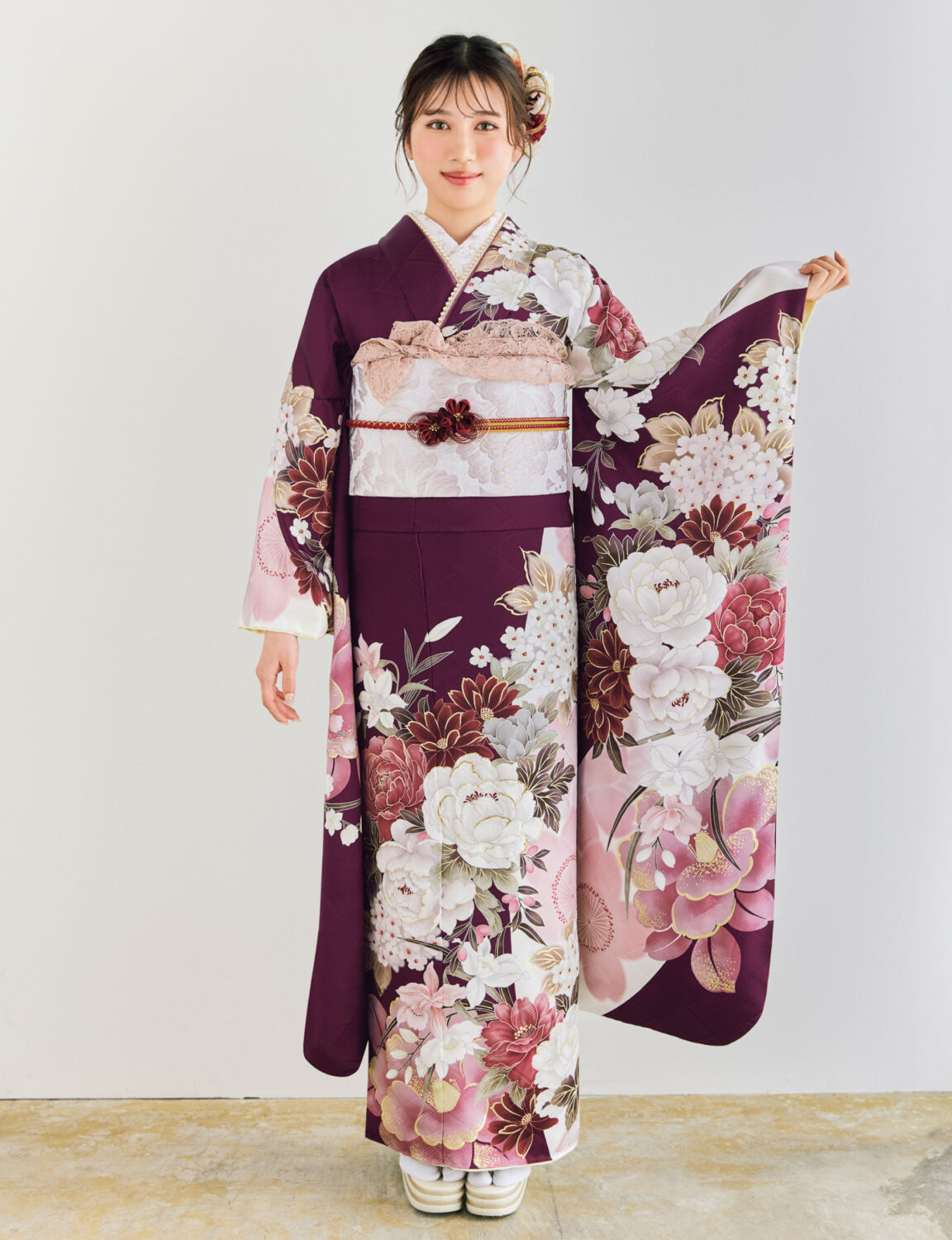 深紫の振袖に白・桃・金の花柄をあしらい、淡色の帯とレース装飾を合わせた女性が、優雅で上品な振袖姿を見せている様子。