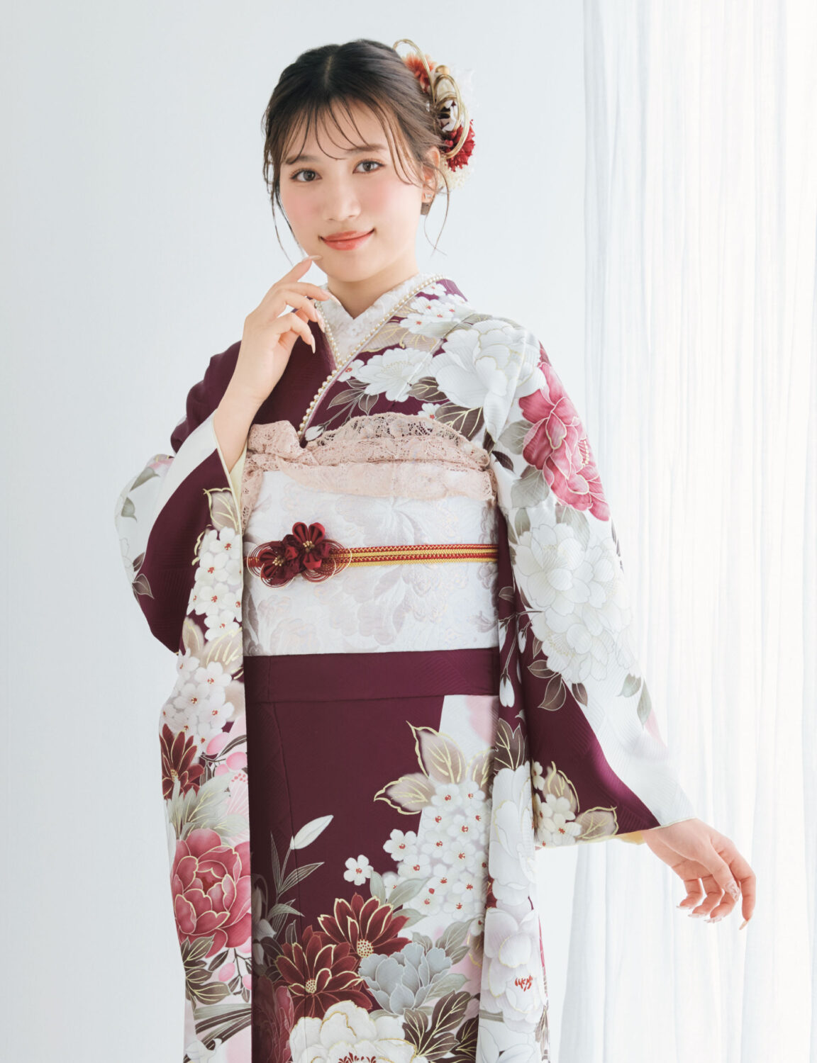 深紫の振袖に白・桃・金の花柄をあしらい、淡色の帯とレース装飾を合わせた女性が、優雅で上品な振袖姿を見せている様子。