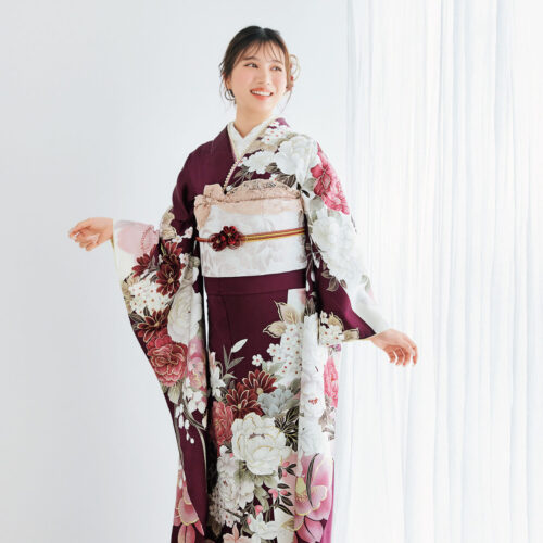 深紫の振袖に白・桃・金の花柄をあしらい、淡色の帯とレース装飾を合わせた女性が、優雅で上品な振袖姿を見せている様子。