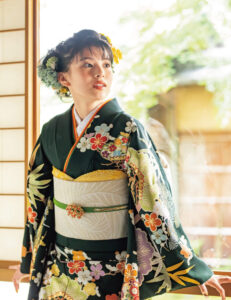 漆黒のごとく深い緑の地に冴える手描き友禅の技。松竹梅の図柄に小付けの草花が舞い、贅を凝らしたカラフルな意匠が豪華さを演出します。