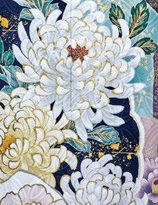 清楚な白と、深みあるスモーキーカラーの取り合わせがおしゃれです。同系色に咲く菊や椿にゴージャスな金箔が映え、印象に残る振袖美人の誕生。