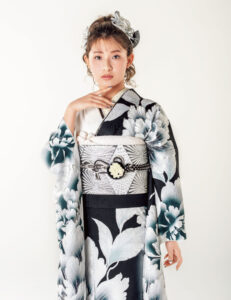 黒と白の振袖に大輪の花模様をあしらい、幾何文様の帯と白の帯締を合わせた女性の立ち姿