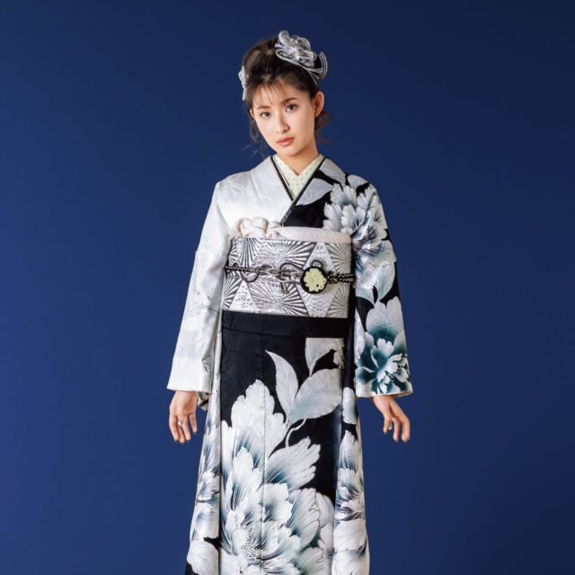 黒と白の振袖に大輪の花模様をあしらい、幾何文様の帯と白の帯締を合わせた女性の立ち姿