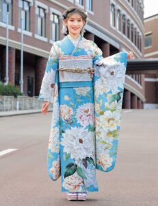 水色の振袖に白牡丹と淡い花々をあしらい、銀灰色の帯と帯締を合わせた女性の立ち姿