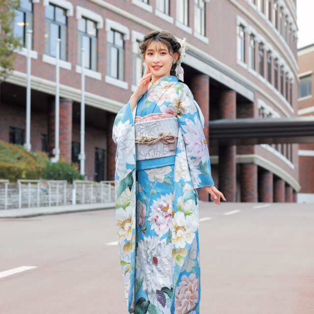水色の振袖に白牡丹と淡い花々をあしらい、銀灰色の帯と帯締を合わせた女性の立ち姿