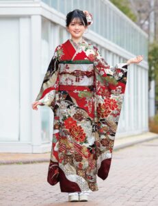 深紅の振袖に牡丹と菊、金彩と幾何文様をあしらい、赤の帯締を合わせた女性の立ち姿