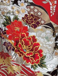 深紅の振袖に牡丹と菊、金彩と幾何文様をあしらい、赤の帯締を合わせた女性の立ち姿