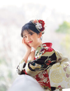 深紅の振袖に牡丹と菊、金彩と幾何文様をあしらい、赤の帯締を合わせた女性の立ち姿