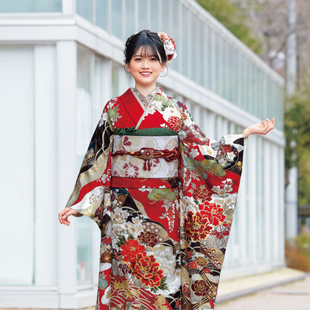深紅の振袖に牡丹と菊、金彩と幾何文様をあしらい、赤の帯締を合わせた女性の立ち姿