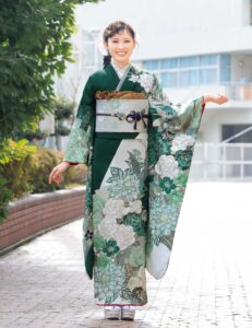 深緑の振袖に白牡丹と菊の花模様をあしらい、金の帯と濃紺の帯締を合わせた女性の立ち姿