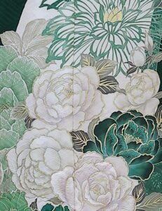 深緑の振袖に白牡丹と菊の花模様をあしらい、金の帯と濃紺の帯締を合わせた女性の立ち姿