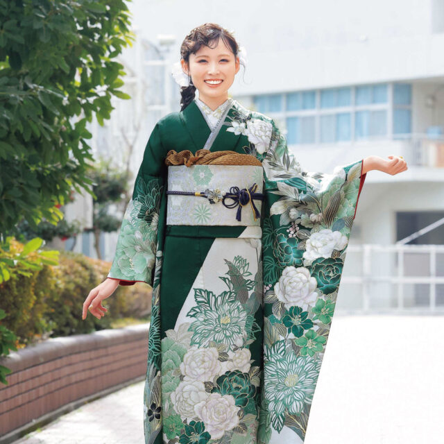 深緑の振袖に白牡丹と菊の花模様をあしらい、金の帯と濃紺の帯締を合わせた女性の立ち姿