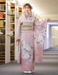紅梅色の振袖に白菊と藤の花模様をあしらい、紫の帯締を合わせた女性の立ち姿