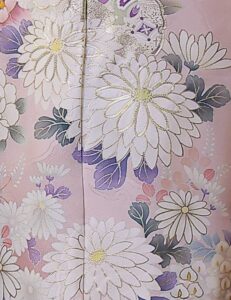 紅梅色の振袖に白菊と藤の花模様をあしらい、紫の帯締を合わせた女性の立ち姿