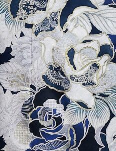 銀白の花模様が描かれた深藍の振袖を着た女性が図書館風の空間に立つ姿。赤の帯締がアクセント。